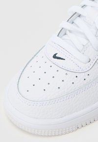 Bijeli kožni tenisice s perforacijama na prstu, ušiveni detalji, bijele vezice i mali crni Nike swoosh logo na remenu.