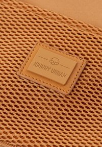 Pomarańczowa siateczkowa tkanina z teksturowaną skórzaną metką z napisem "JOHNNY URBAN". Akcenty w postaci wzoru klucza zapewniają wentylację. Prostokątny kształt.