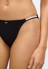 Μαύρο κάτω μέρος μπικίνι με λεπτή χρυσή λεπτομέρεια, διακοσμημένο με λευκές και μ�αύρες ρίγες. Απαλή υφή υφάσματος και σχεδίαση ελάχιστης κάλυψης.