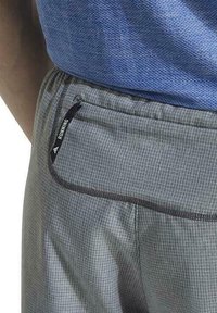 Pantalones cortos de running grises hechos de material ligero, con un bolsillo con cremallera y una etiqueta negra con la palabra "RUNNING", además de un diseño de patrón de cuadrícula.
