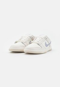 Een paar lage witte sneakers met lichtgrijze Nike swoosh-logo's en witte veters op een effen witte achtergrond.