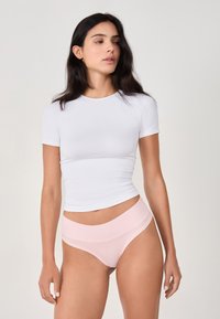 T-shirt bianco aderente con maniche corte abbinato a mutandine alte color rosa chiaro. Tessuto liscio con una consistenza morbida, design minimal.