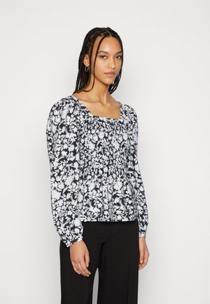 Blusa floral em preto e branco com mangas longas, decote quadrado e detalhes franzidos na cintura, combinada com calças pretas.