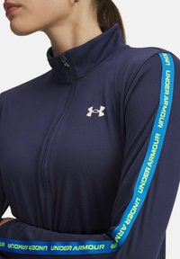 Navy half-zip pullover made of moisture-wicking fabric, featuring a silver logo and blue-green stripes with "UNDER ARMOUR" text on the sleeves.