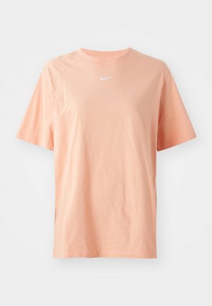 Perzikkleurig katoenen T-shirt met korte mouwen, ronde hals en een wit Nike-logo op de borst. Zachte textuur, losse pasvorm en geen patronen.