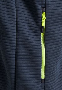 Tissu texturé bleu marine avec nervures verticales, doté d'une fermeture éclair vert néon vif. Comprend un curseur de fermeture éclair noir et des détails accentués.