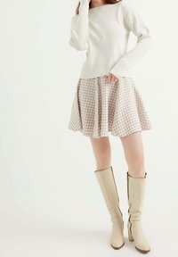 Pletený krémový svetr, kostkovaná béžová a bílá rozšířená sukně a béžové kozačky ke kolenům s bočním zipem. Hladké textury po celé ploše.