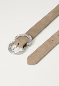 Beige ruskindebælte med en stor sølv cirkulær spænde. Remmen har en glat tekstur med pladserede huller til justering.