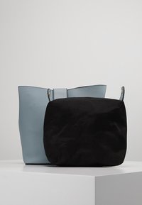 Grote lichtblauwe lederen schoudertas met een gestructureerde afwerking, voorzien van een kleinere zwarte suède pouch die met straps is vastgemaakt.