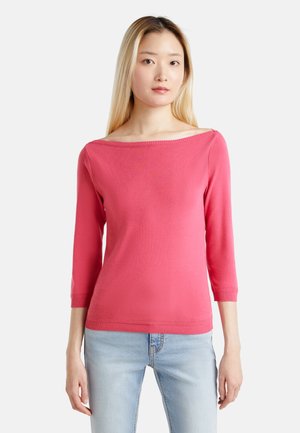 Maglione rosa a maglia con scollatura ampia, maniche a tre quarti e orlo a coste. Indossato con jeans blu chiaro. Texture liscia.