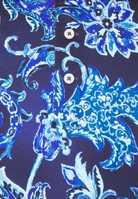 Námorníková tkanina s modrým květinovým vzorem. Obsahuje složité vzory a dva bílé knoflíky poblíž výstřihu. Hladká textura.