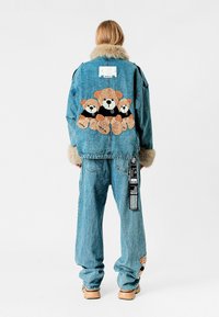 Chaqueta de mezclilla con cuello de piel, con osos de peluche bordados en la parte posterior. Combinada con pantalones de mezclilla holgados y una etiqueta.