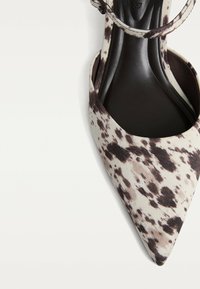 Pointed-toe slingback shoe in fabric with a black and beige spotted pattern. Features a slender ankle strap and a smooth black interior.
