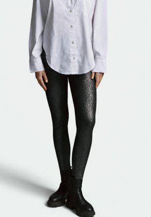 Black leggings with a shiny texture, featuring a subtle glitter pattern. Paired with a white button-up shirt and black ankle boots.