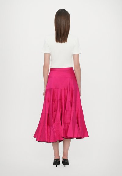 Jupe en satin rose à volants avec un ourlet évasé, associée à un top blanc ajusté. La jupe présente une texture lisse et une taille simple.