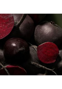 Remolachas de color púrpura intenso con piel rugosa y raíces visibles, algunas cortadas para mostrar la pulpa roja interior rica. Textura mate con imperfecciones naturales.