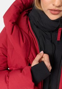 Red puffer jacket with a black interior, featuring a high collar, front zipper, and ribbed black cuffs. The texture appears smooth and insulated.