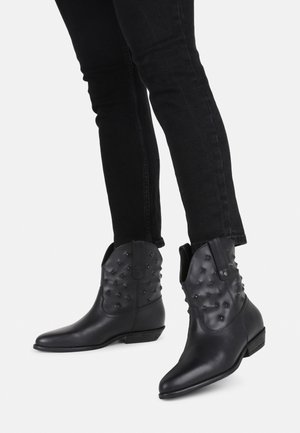 Black leather ankle boots featuring studded detailing, pointed toe, and a low stacked heel. Paired with black fitted jeans.