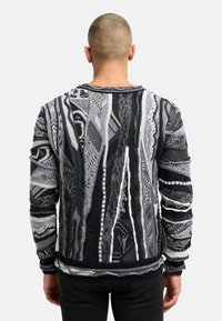 Pull en noir et blanc avec un motif, doté de rayures texturées, utilisant différentes techniques de tricot, et avec un col et des poignets côtelés.