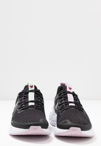 Chaussures de sport noires avec un dessus en mesh, des lacets en accent menthe et rose, des semelles intermédiaires texturées et des semelles extérieures en caoutchouc blanc. Logo Nike visible.