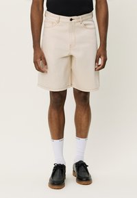 Shorts de mezclilla beige con costuras visibles, diseño clásico de cinco bolsillos y corte recto, combinados con zapatos negros y calcetines blancos.