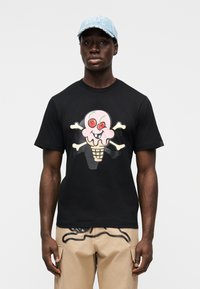 Μαύρο βαμβακερό t-shirt με πολύχρωμο σχέδιο παγωτού και οστά κρανίου σε σταυρό. Φορεμένο με μπεζ παντελόνι κάργκο, παρουσιάζοντας μοναδικά σχέδια.