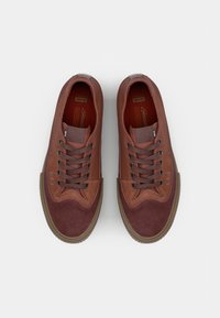 Brązowe sneakersy z kombinacją gładkich i zamszowych tekstur, sześcioma oczkami, ciemnobrązowymi sznurówkami oraz gumową podeszwą z wzorzystym bieżnikiem.