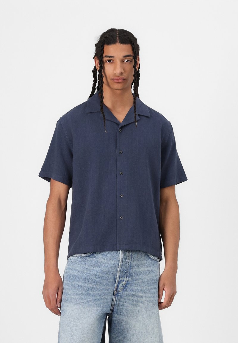 Navy short-sleeve button-up shirt with a classic collar, made from a textured fabric, featuring six black buttons and a relaxed fit.