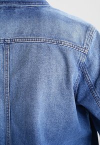 Džínová bunda světle modré barvy s klasickým střihem, špičatým límcem, prošitými švy a mírně vybledlou texturou.