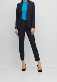 Traje marinero con chaqueta ajustada y pantalones de corte slim, combinado con un top azul de canalé y tacones negros puntiagudos. Tejido suave, diseño elegante.