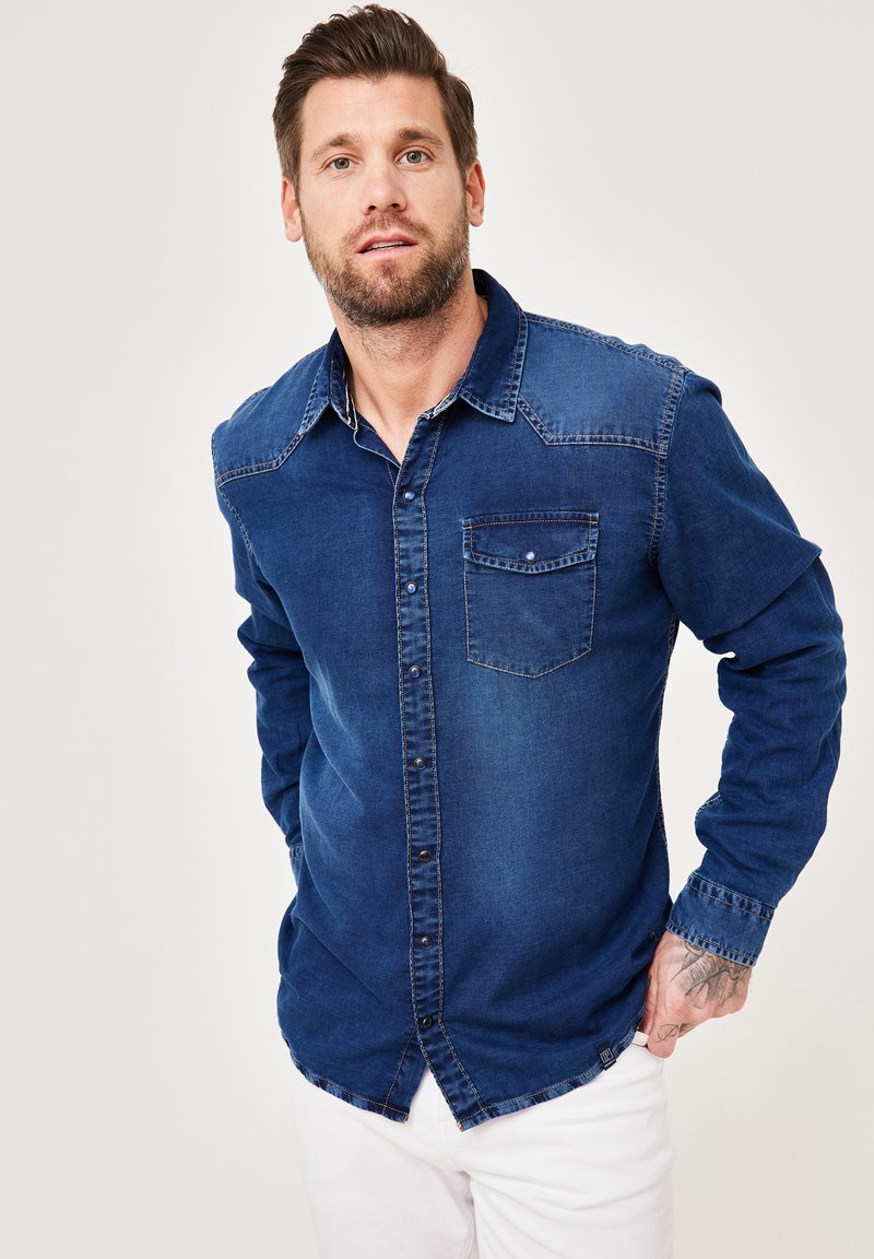 Dunkelblaus Denimhemd mit Knopfverschluss, zwei Brusttaschen und kontrastreichen, helleren Details an Schultern und Kragen.