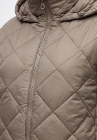 Veste matelassée taupe avec couture en losange, fermeture éclair centrale et capuche attachée avec cordon réglable.