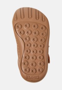 Sole in gomma marrone con motivi a grip circolari, texture liscia e indentazioni laterali; presenta il nome del marchio impressa sul fondo.