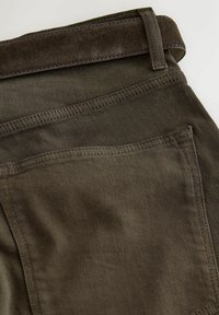 Pantalon en denim marron avec poche arrière visible et ceinture en suédine marron assortie passée dans les passants.
