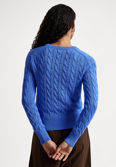 Spīdīgi zilas krāsas adīts džemperis ar pītās adījuma rakstu, elastīgu apakšmala un aproču ribojumu. Džemperim ir apaļa kakla izgriezums un teksturēts raksts visā audumā.