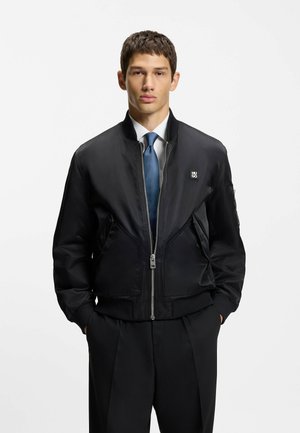 Black bomber jacket made of smooth fabric, featuring a zip front, ribbed cuffs, two side pockets, and a small logo on the chest.