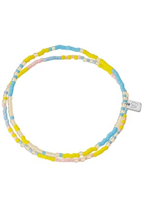 Nahaufnahme eines Handgelenks mit einem filigranen Perlenarmband in Gelb, Blau und Pink, getragen von einer Person mit weißem Oberteil, Hand nahe am Kinn.