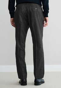 Men's dark gray striped trousers; tailored fit, two back pockets with buttons, flat front, fabric surface with vertical pinstripes, worn with black shoes.