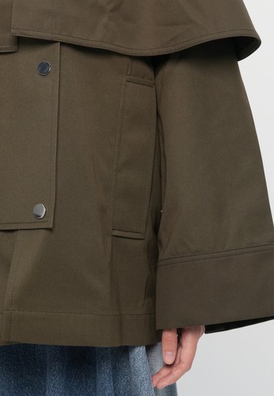 Olive-green jacket with a wide collar, large front buttons, flap pockets, and a textured fabric. Features a loose, structured fit and wide sleeves.