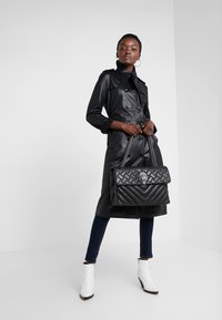 Czarny płaszcz trench z ekoskóry z podwójnymi guzikami, w połączeniu z pikowaną czarną torebką na ramię z srebrnym łańcuchem i akcentami.