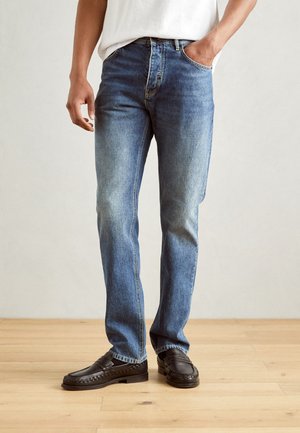 Blue denim jeans with a straight leg fit, faded color, classic five-pocket design, and stitched details, paired with black loafers.
