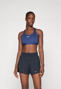 Soutien-gorge de sport bleu marine avec un logo Nike blanc, associé à un short de sport noir avec des fentes latérales et une taille élastique.