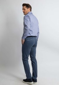 Lichtblauw geruit overhemd met lange mouwen, gecombineerd met donkerblauwe strakke broek en zwarte sneakers.