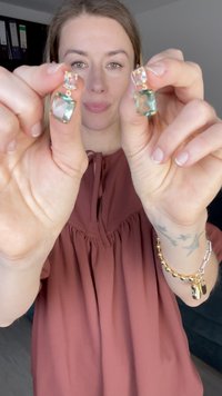 Naušnice u zlatnoj boji s prozirnim i zelenim pravokutnim kamenjem, svaki s malim okruglim detaljima, koje prikazuju geometrijski dizajn.