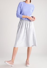 Jasnofioletowy sweter z długim rękawem, szara plisowana spódnica midi oraz blade różowe sneakersy. Gładkie tekstury i luźny krój przez cały czas.