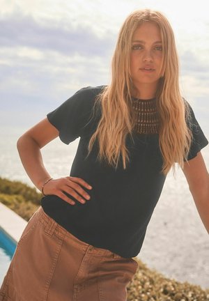 Svart t-shirt med kort ärm och en strukturerad, vävd krage, tillsammans med en ljusbrun knälång kjol med diskreta fickor.