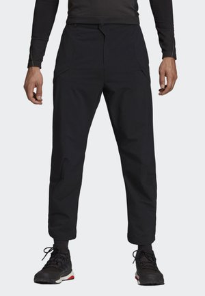 Zwarte tapered pants met een gladde textuur, voorzien van zijzakken en elastische boorden. Gecombineerd met zwarte schoenen en een aansluitend topje.