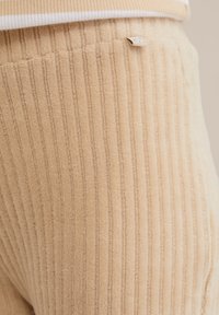 Beige ribbed fabric, textured with vertical lines. Featured label on side. Soft, plush material, enhancing visual depth and dimension.