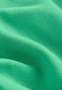Tessuto morbido e leggero di un brillante verde con una sottile trama testurizzata e superficie liscia, che mostra pieghe e ondulazioni delicate.