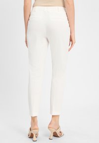 Weiße maßgeschneiderte Hosen mit schmaler Passform, glattem Textil und zwei Gesäßtaschen. Kombiniert mit hellen, hochhackigen Mules.